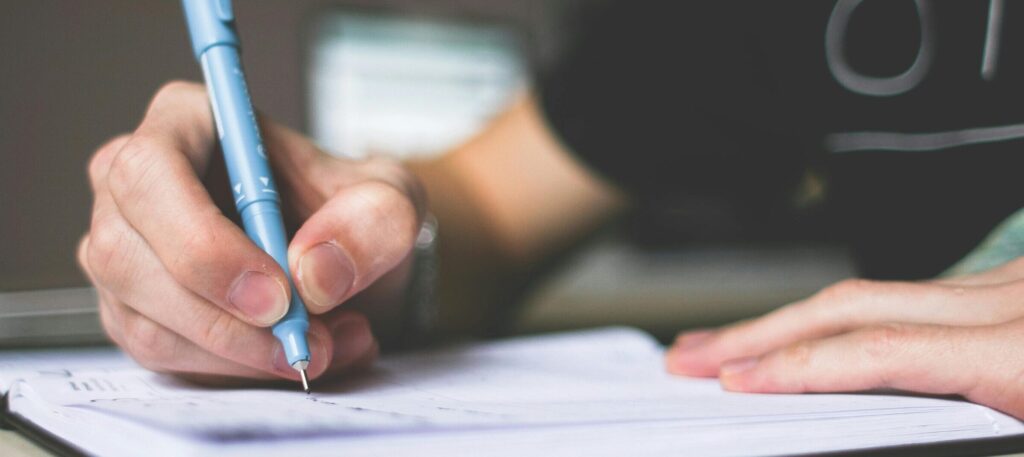 Close-up of hand writing in notebook using a blue pen, focus on creativity.
