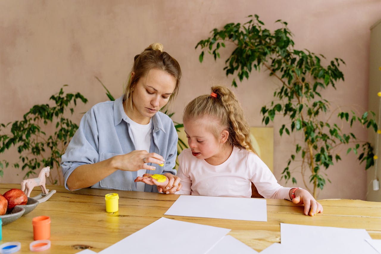 A mother and daughter engage in creative finger painting at a table indoors.